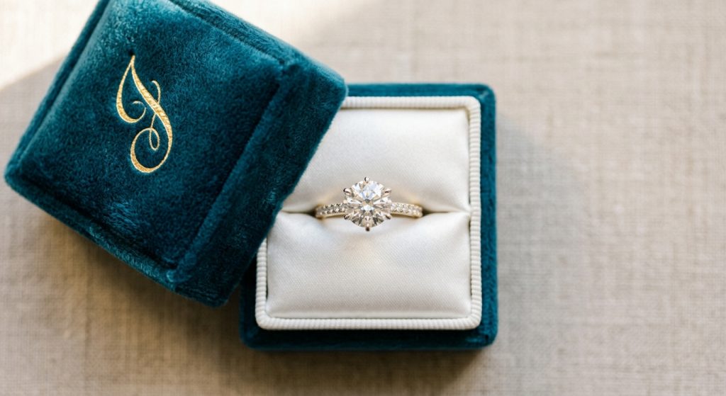 Estuche de terciopelo azul verdoso abierto con un anillo de diamantes en su interior