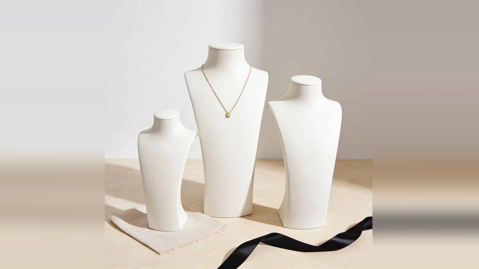 Tres petos forrados blancos de la serie Alejandría con un collar sobre tela beige