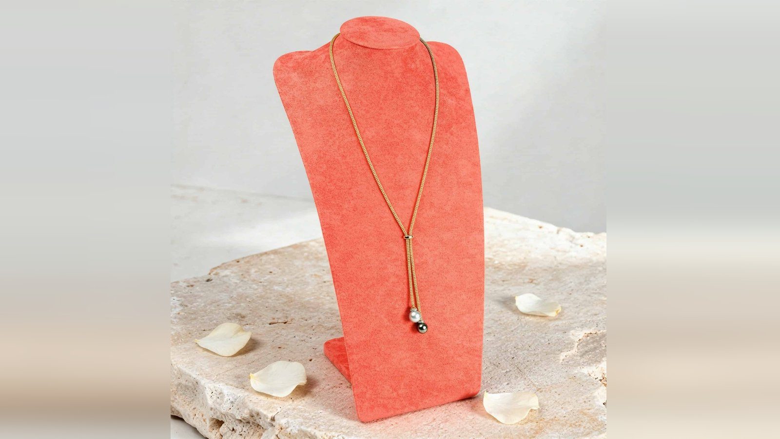 Peto forrado presentando un collar sobre una losa de piedra con flores blancas